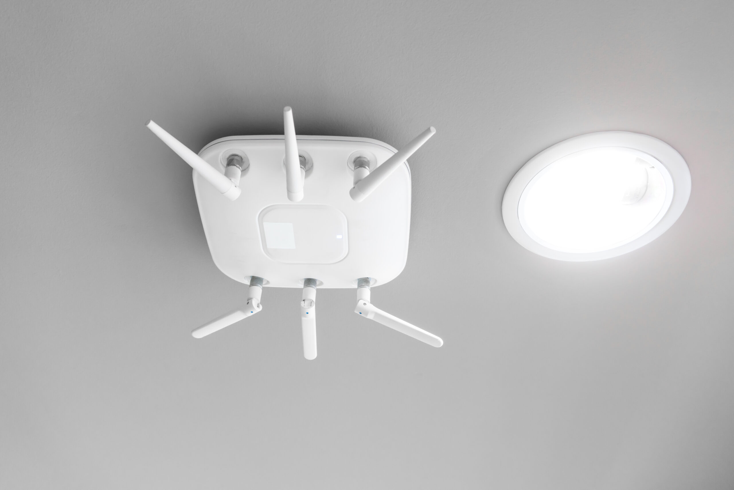 Wireless router for network hanging on white ceiling near circle LED down light. World wide network technology.